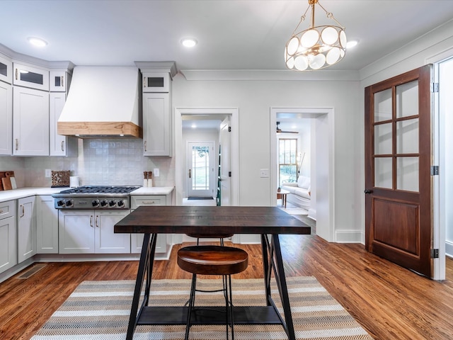 kitchen featuring hanging light fixtures, decorative backsplash, custom range hood, white cabinetry, and stainless steel gas cooktop