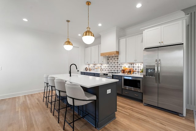 kitchen with white cabinets, sink, an island with sink, appliances with stainless steel finishes, and custom range hood