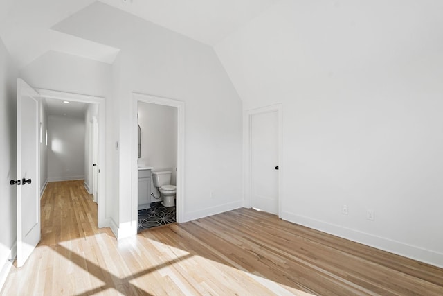 unfurnished bedroom with lofted ceiling, connected bathroom, and light hardwood / wood-style flooring