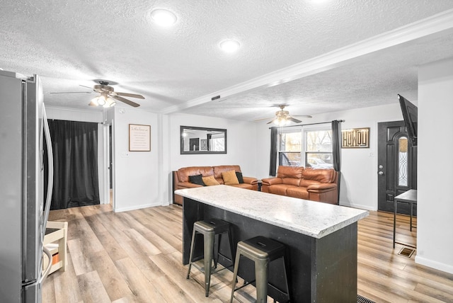 kitchen with a kitchen bar, stainless steel fridge, light hardwood / wood-style flooring, and a textured ceiling