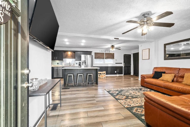 living room with ceiling fan, light wood-type flooring, and a textured ceiling