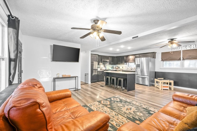 living room with a textured ceiling, light wood-type flooring, ceiling fan, and sink