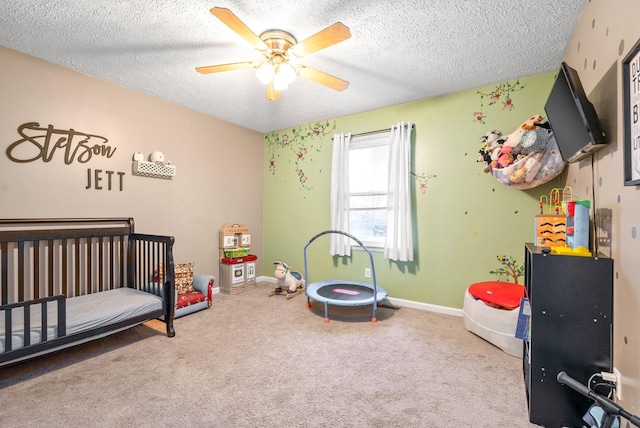 bedroom featuring carpet flooring, a textured ceiling, a nursery area, and ceiling fan