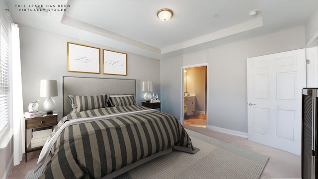 carpeted bedroom featuring a tray ceiling and ensuite bath