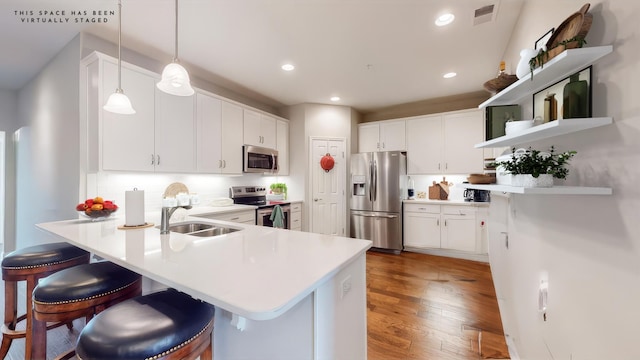 kitchen featuring appliances with stainless steel finishes, pendant lighting, white cabinetry, a breakfast bar area, and kitchen peninsula