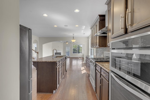 kitchen featuring ceiling fan, sink, stone countertops, a kitchen island with sink, and appliances with stainless steel finishes