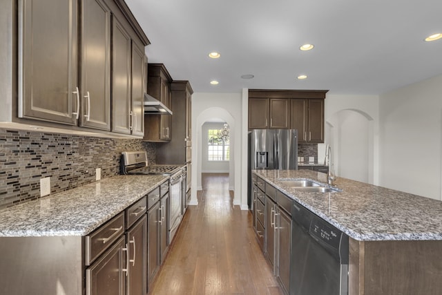 kitchen with dark brown cabinets, stainless steel appliances, a kitchen island with sink, exhaust hood, and sink