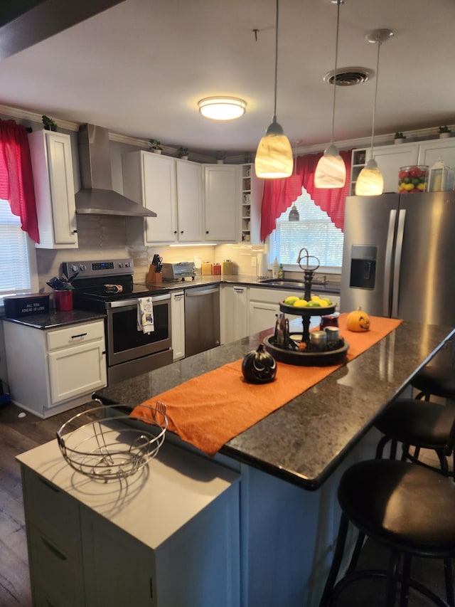 kitchen featuring white cabinetry, hanging light fixtures, wall chimney range hood, and appliances with stainless steel finishes