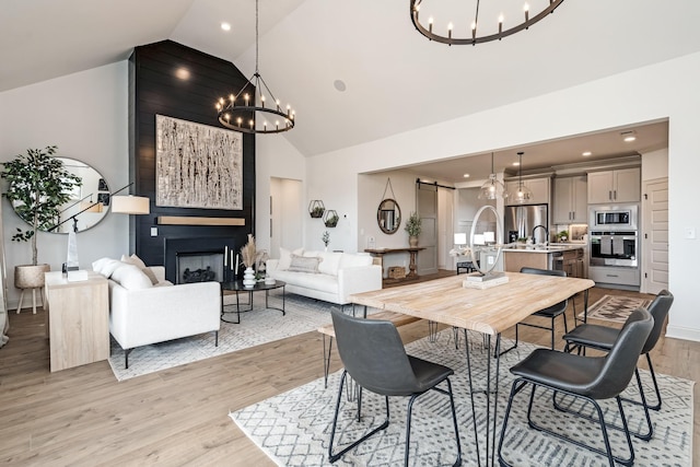 dining area with sink, vaulted ceiling, light wood-type flooring, a notable chandelier, and a large fireplace