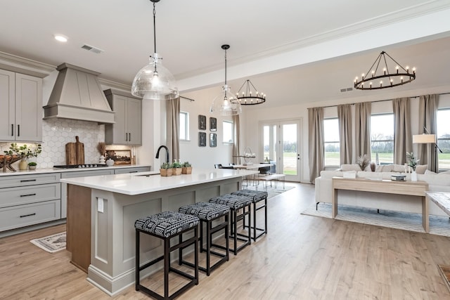 kitchen featuring decorative backsplash, custom range hood, sink, a center island with sink, and gray cabinets