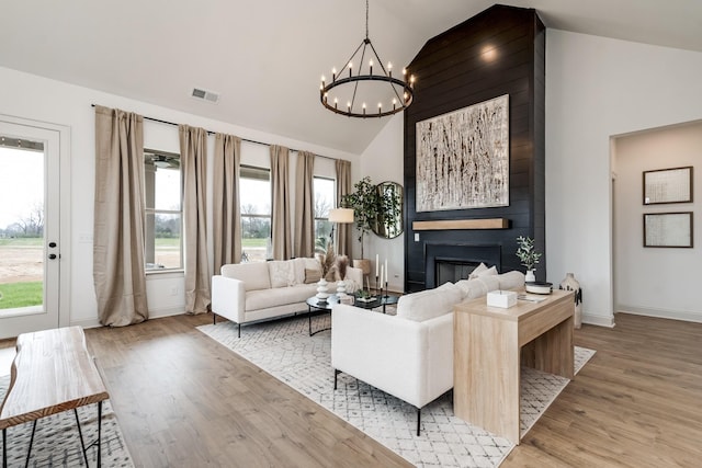 living room with light wood-type flooring, a large fireplace, a chandelier, and vaulted ceiling