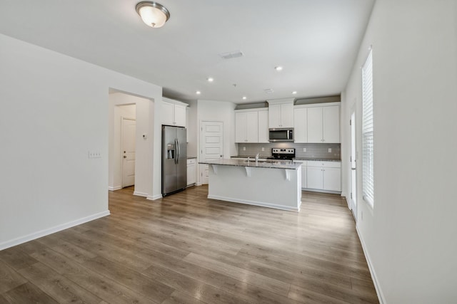 kitchen featuring tasteful backsplash, an island with sink, a kitchen bar, white cabinets, and appliances with stainless steel finishes