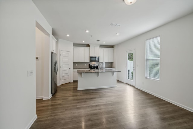 kitchen featuring appliances with stainless steel finishes, a breakfast bar, a kitchen island with sink, dark hardwood / wood-style floors, and white cabinetry