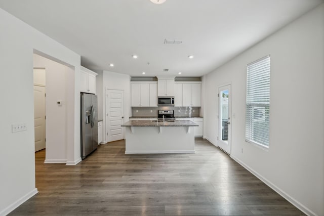 kitchen with appliances with stainless steel finishes, dark stone counters, a kitchen island with sink, dark wood-type flooring, and white cabinetry