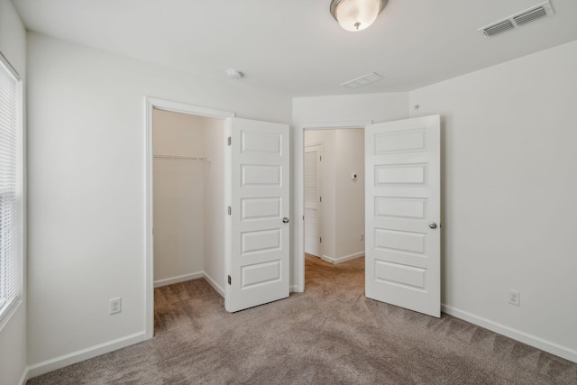 unfurnished bedroom featuring a walk in closet, light carpet, and a closet