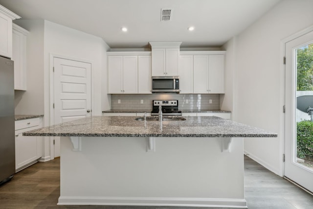 kitchen with white cabinets, an island with sink, stainless steel appliances, and stone countertops