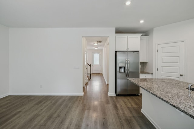 kitchen featuring light stone countertops, stainless steel fridge, white cabinetry, and dark wood-type flooring