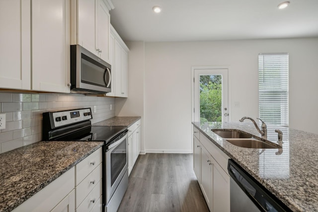 kitchen with appliances with stainless steel finishes, backsplash, sink, dark stone countertops, and white cabinets