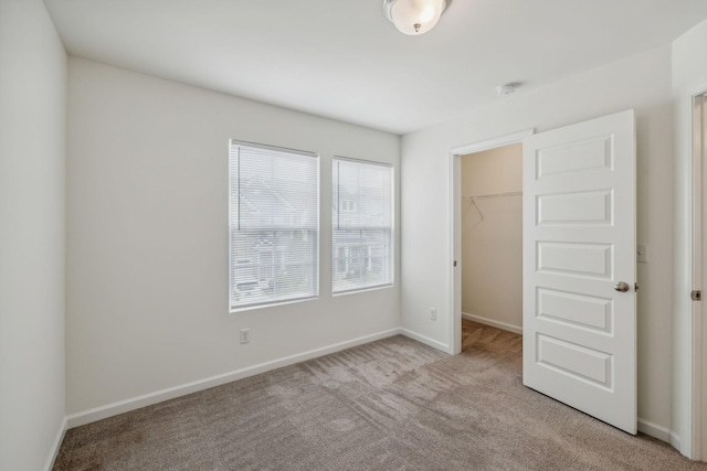 unfurnished bedroom with a walk in closet, light carpet, and a closet