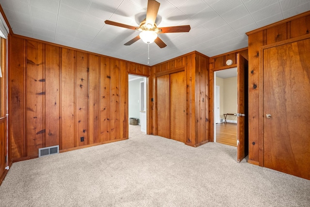 unfurnished bedroom featuring light colored carpet, ceiling fan, and wooden walls