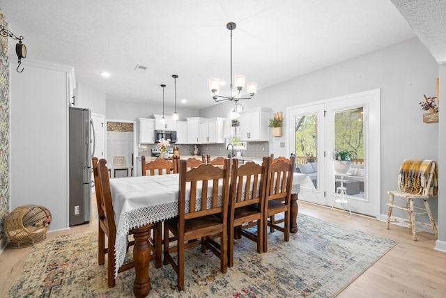 dining area featuring sink, light hardwood / wood-style flooring, a textured ceiling, and a notable chandelier