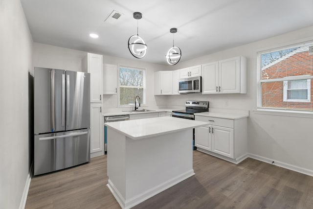 kitchen featuring white cabinetry, sink, a center island, pendant lighting, and appliances with stainless steel finishes