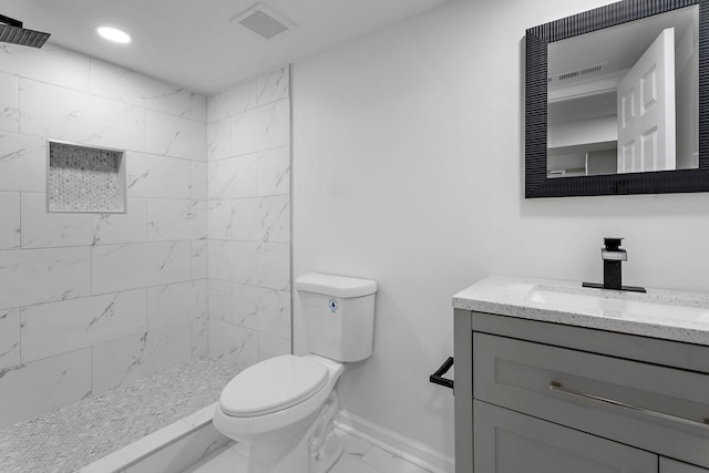 bathroom featuring a tile shower, vanity, and toilet