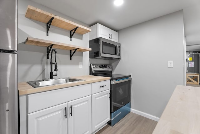 kitchen featuring wooden counters, light wood-type flooring, stainless steel appliances, sink, and white cabinetry