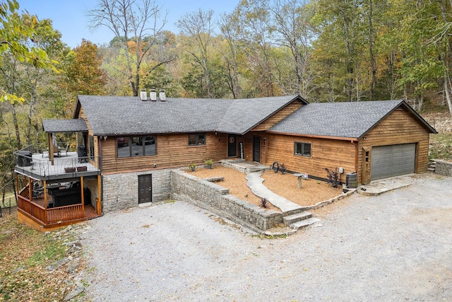 rustic home with a garage, driveway, a shingled roof, and central AC