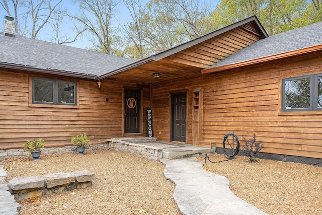 entrance to property with a shingled roof and a chimney