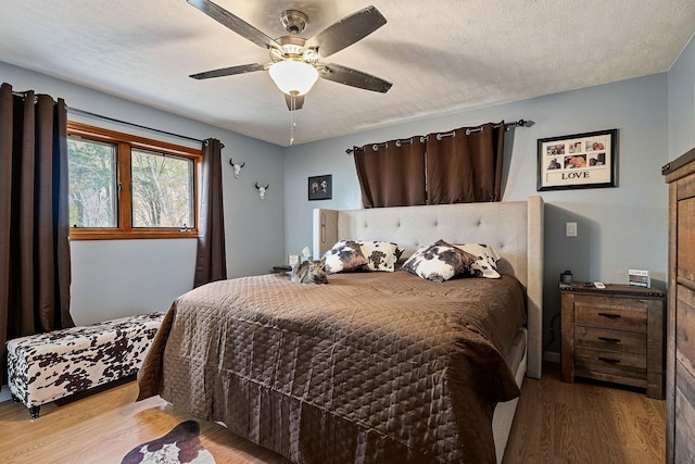 bedroom with light wood-type flooring, ceiling fan, and a textured ceiling