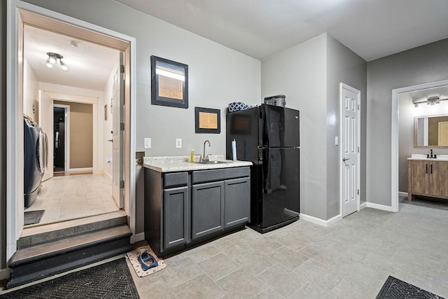 kitchen featuring light stone counters, a sink, freestanding refrigerator, and baseboards