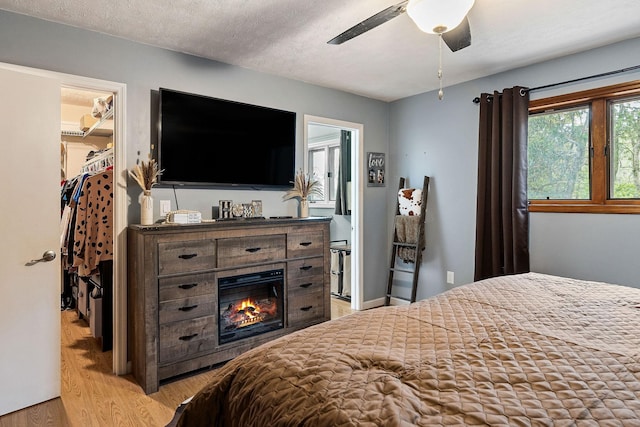 bedroom with a textured ceiling, light wood-style floors, a closet, a walk in closet, and a glass covered fireplace