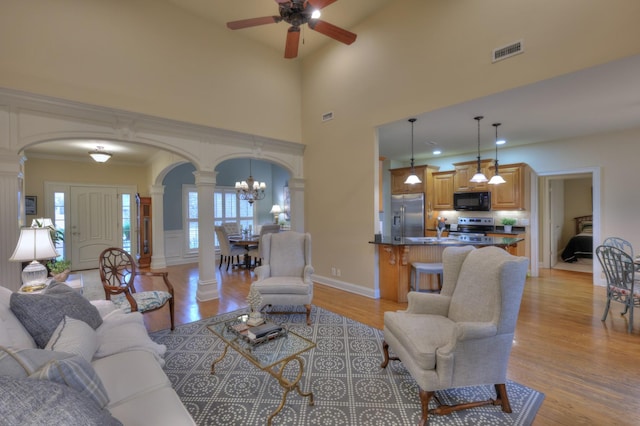 living room with ornate columns, ceiling fan with notable chandelier, and light wood-type flooring