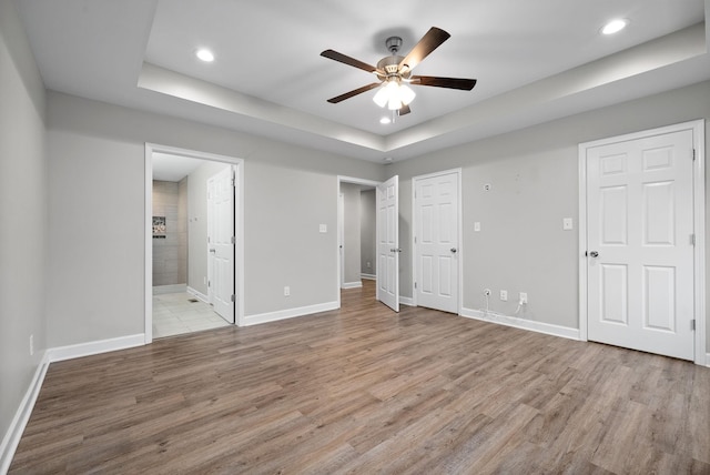 unfurnished bedroom with light wood-type flooring, a tray ceiling, ceiling fan, and ensuite bathroom