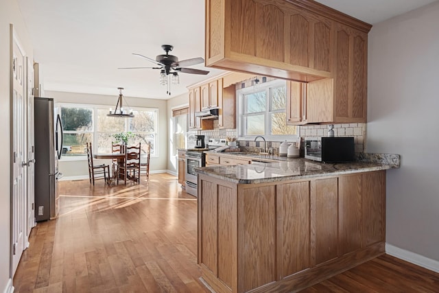 kitchen featuring dark stone countertops, stainless steel appliances, tasteful backsplash, kitchen peninsula, and light wood-type flooring