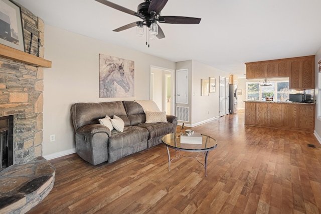 living room with dark wood-type flooring, ceiling fan, and a stone fireplace