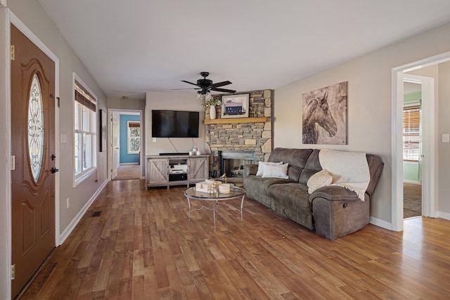 living room with hardwood / wood-style floors, a stone fireplace, and ceiling fan