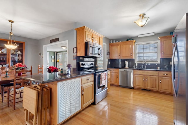 kitchen featuring appliances with stainless steel finishes, tasteful backsplash, sink, decorative light fixtures, and light hardwood / wood-style floors