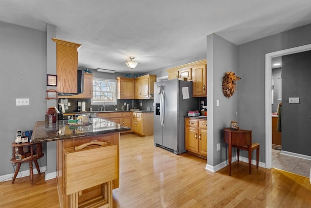 kitchen featuring stainless steel fridge with ice dispenser, backsplash, kitchen peninsula, dark stone counters, and a kitchen bar