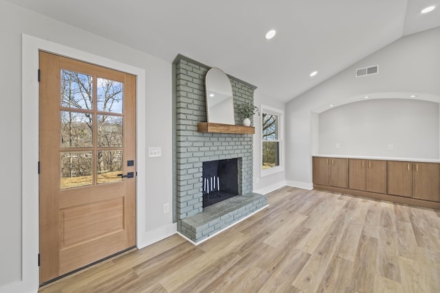 unfurnished living room with visible vents, a fireplace, light wood-type flooring, and vaulted ceiling