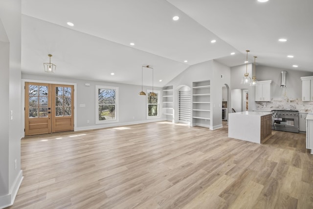 unfurnished living room featuring built in shelves, baseboards, arched walkways, vaulted ceiling, and light wood-style floors