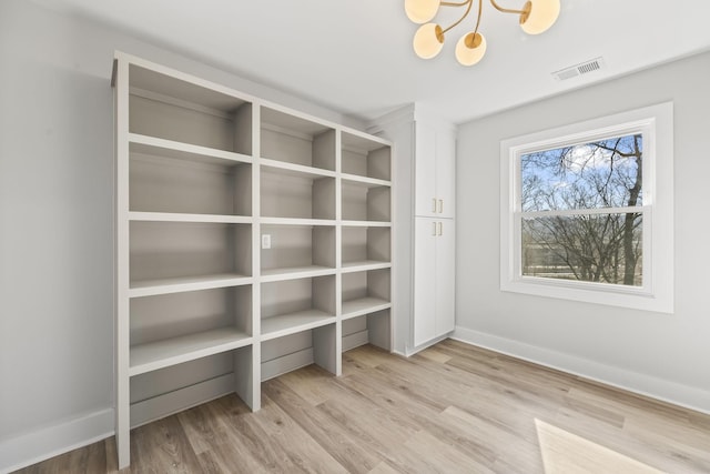 interior space featuring light wood-type flooring, visible vents, baseboards, and an inviting chandelier