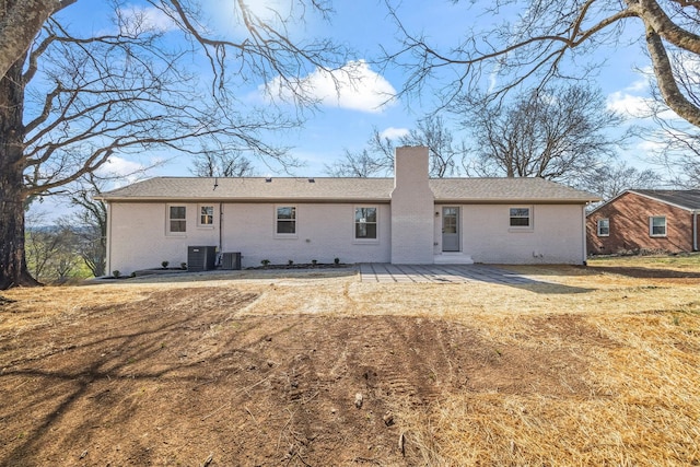 back of house with brick siding, central AC unit, and a chimney