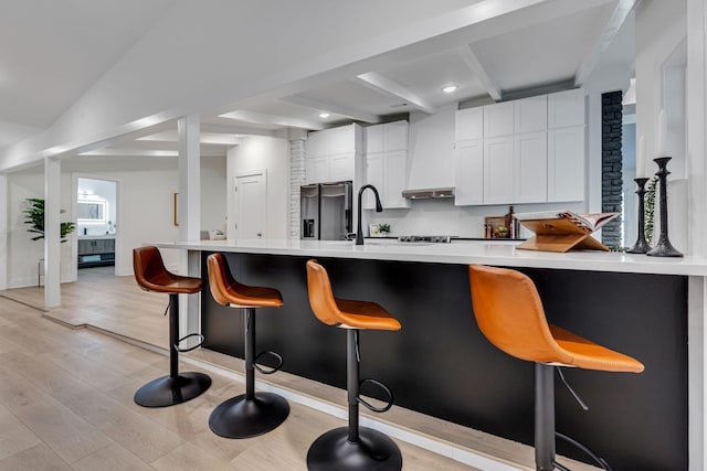 kitchen with white cabinetry, custom range hood, light hardwood / wood-style floors, a kitchen bar, and kitchen peninsula