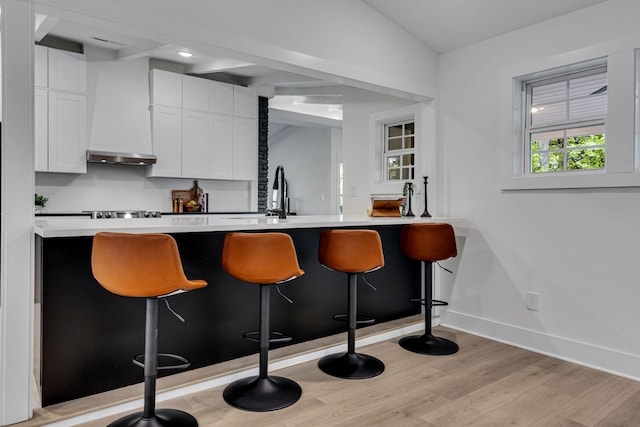 bar featuring ventilation hood, sink, light hardwood / wood-style floors, white cabinetry, and gas cooktop