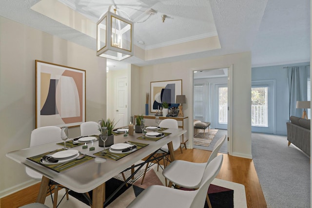 dining space featuring ornamental molding, a textured ceiling, a tray ceiling, light hardwood / wood-style flooring, and a chandelier