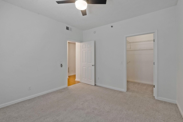 unfurnished bedroom featuring a spacious closet, a closet, ceiling fan, and light colored carpet