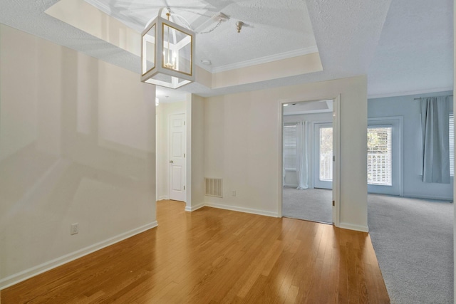 unfurnished living room featuring a raised ceiling, ornamental molding, a textured ceiling, and hardwood / wood-style flooring