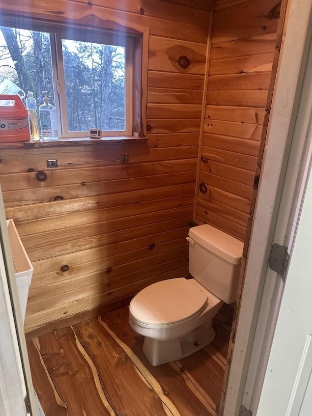 bathroom with toilet, wood-type flooring, and wood walls